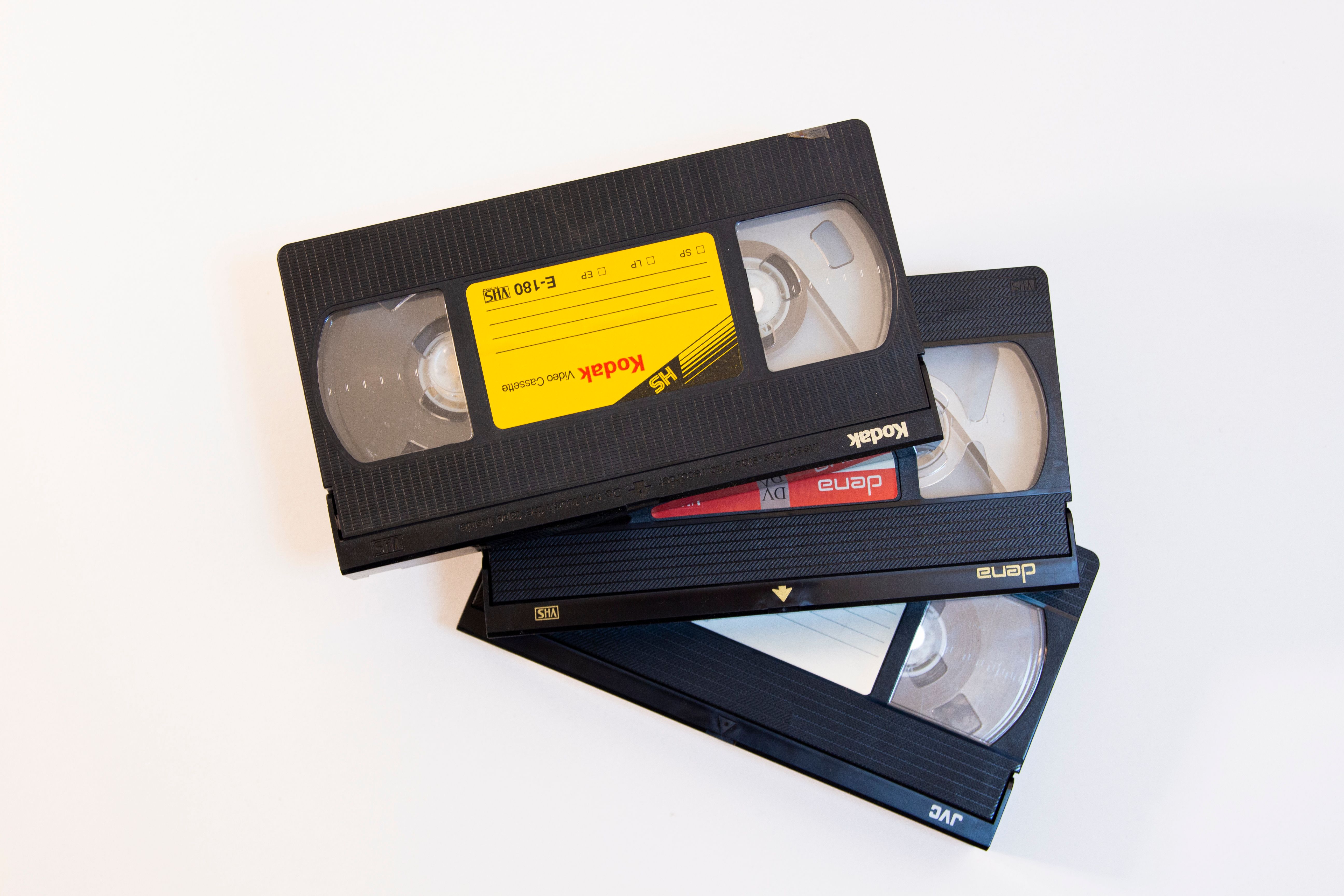 Close-up of a stack of vintage VHS video cassette tapes on a white background, symbolizing nostalgia.