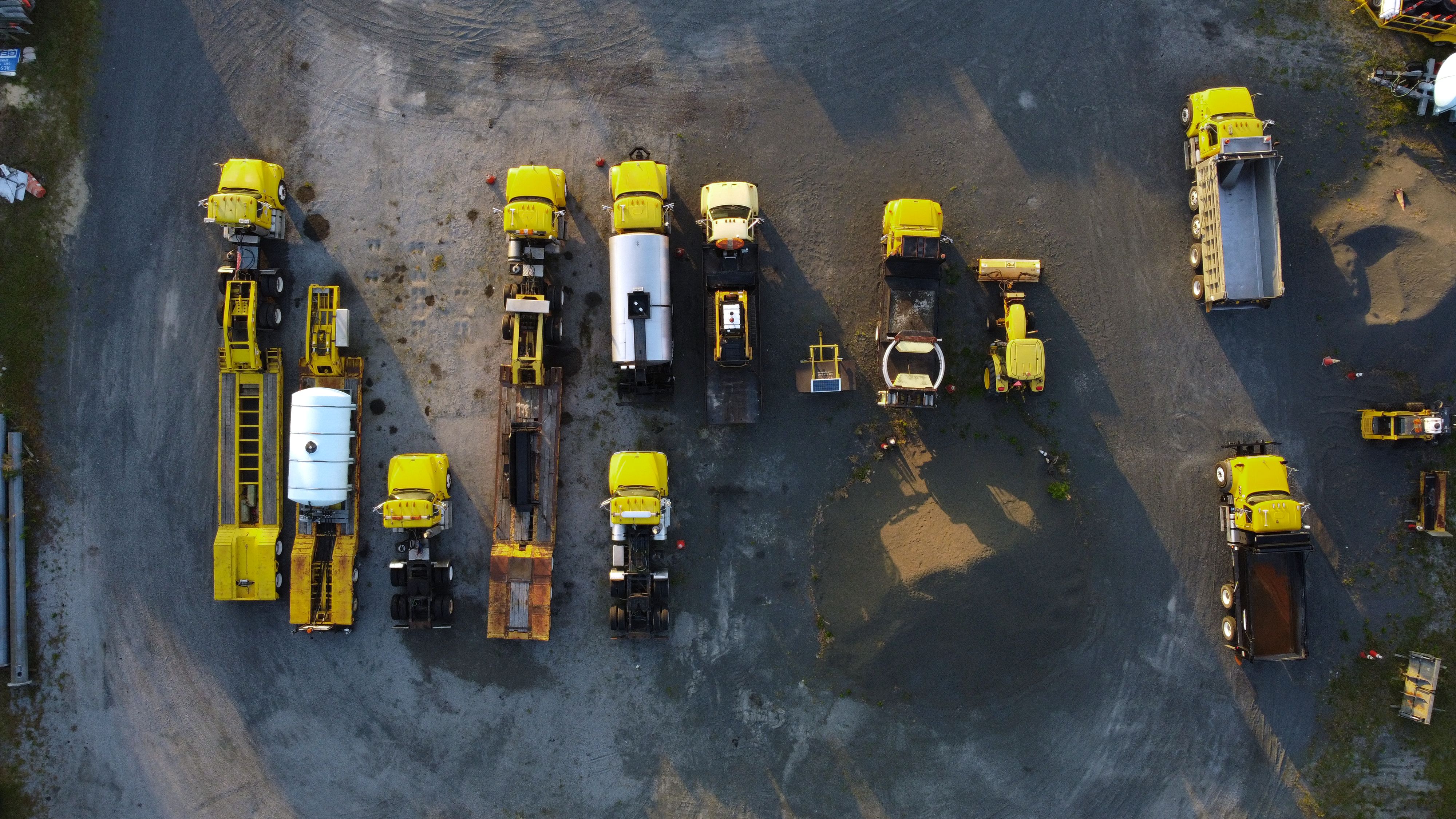 Overhead view of yellow construction trucks parked in neat rows on a gravel surface.