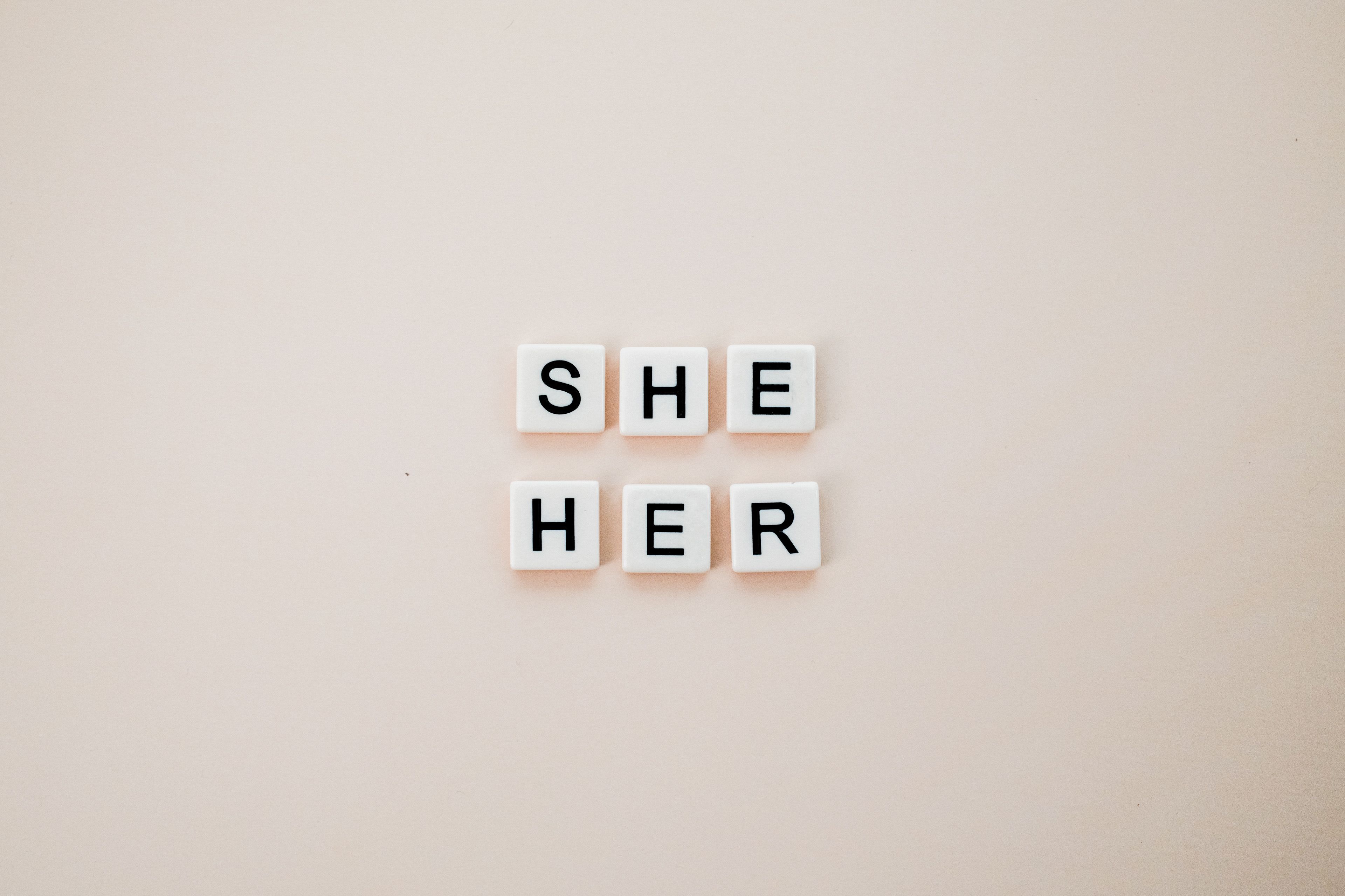 Minimalist photo of letter tiles spelling She Her on a neutral background.