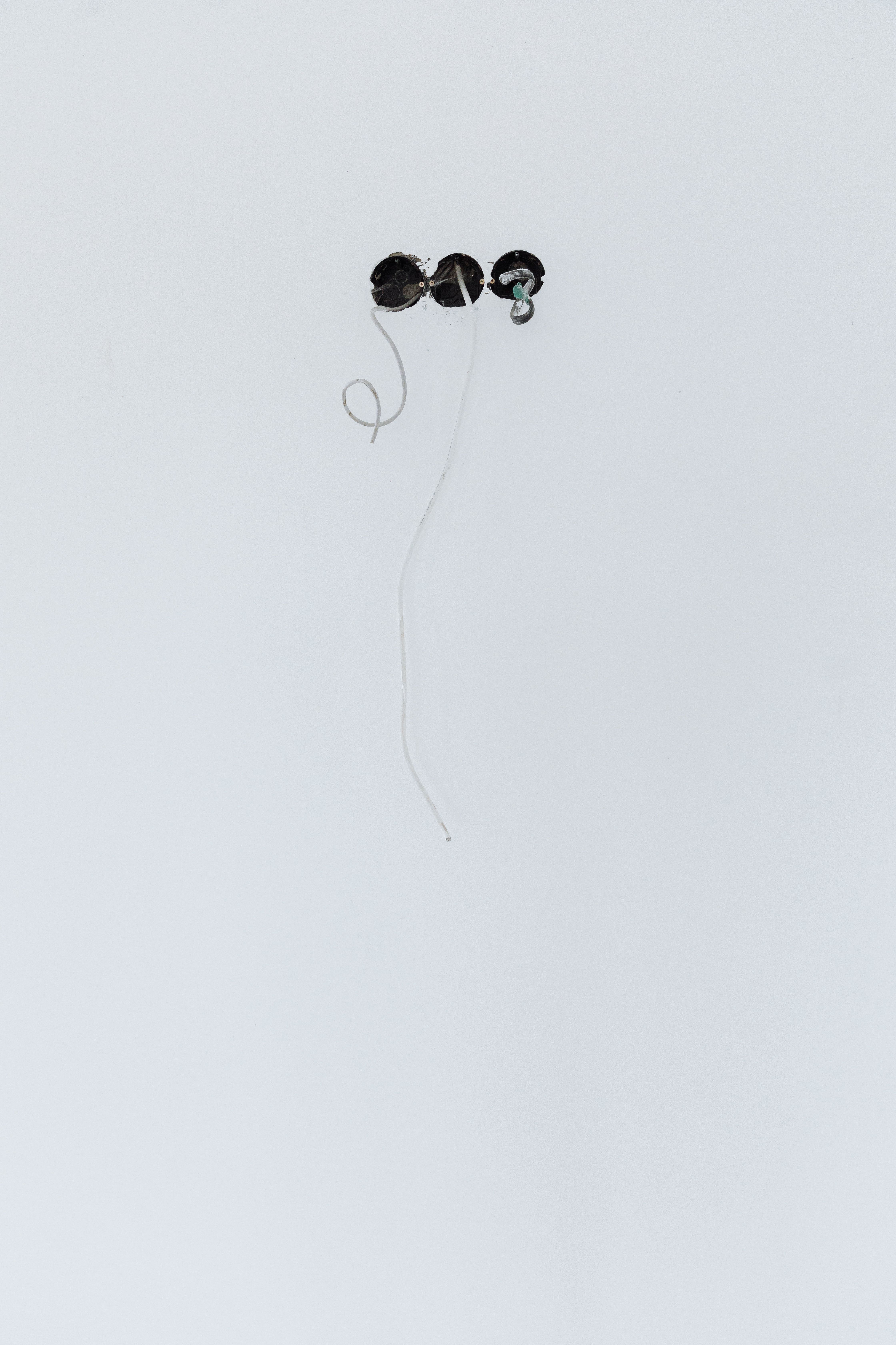 Close-up of wires emerging from holes in a white wall, showcasing electrical installation.